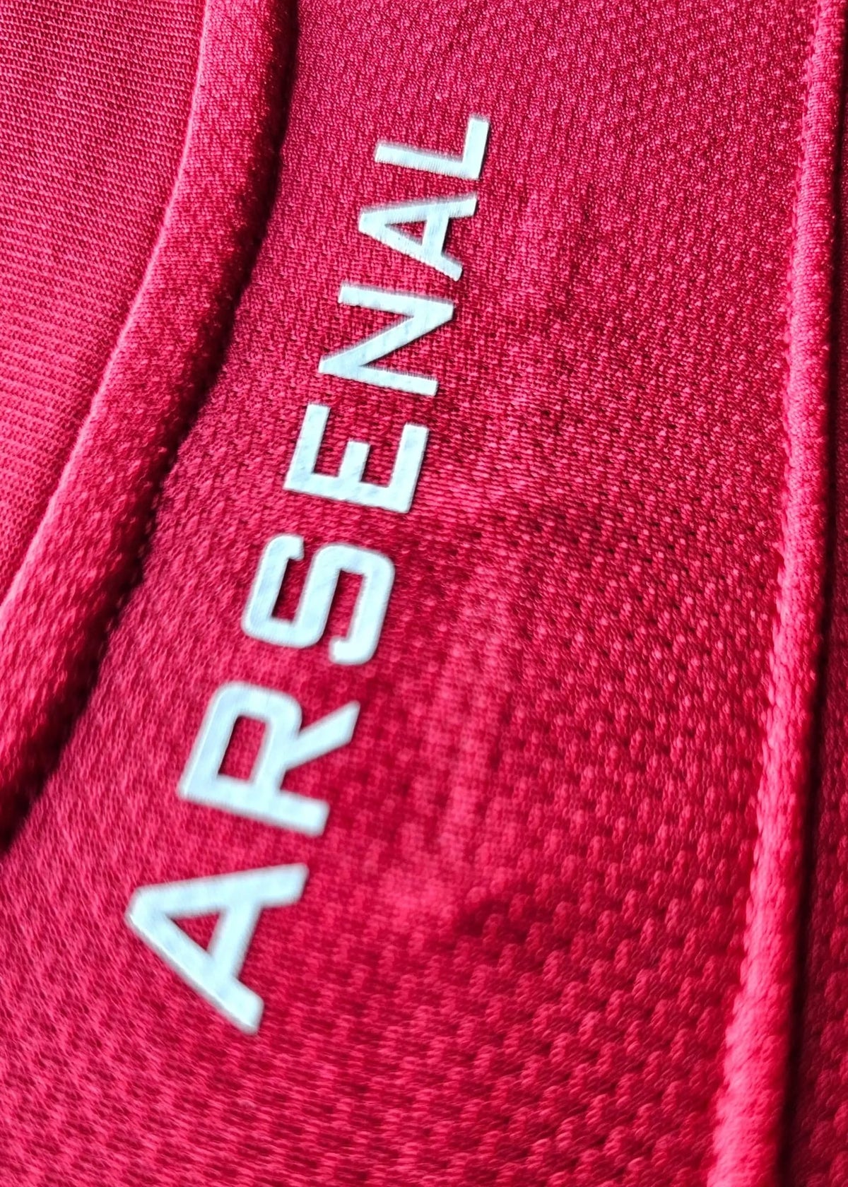 Close-up of the white ARSENAL wordmark near the collar seam of Robin van Persie's red Arsenal Champions League No. 10 shirt.