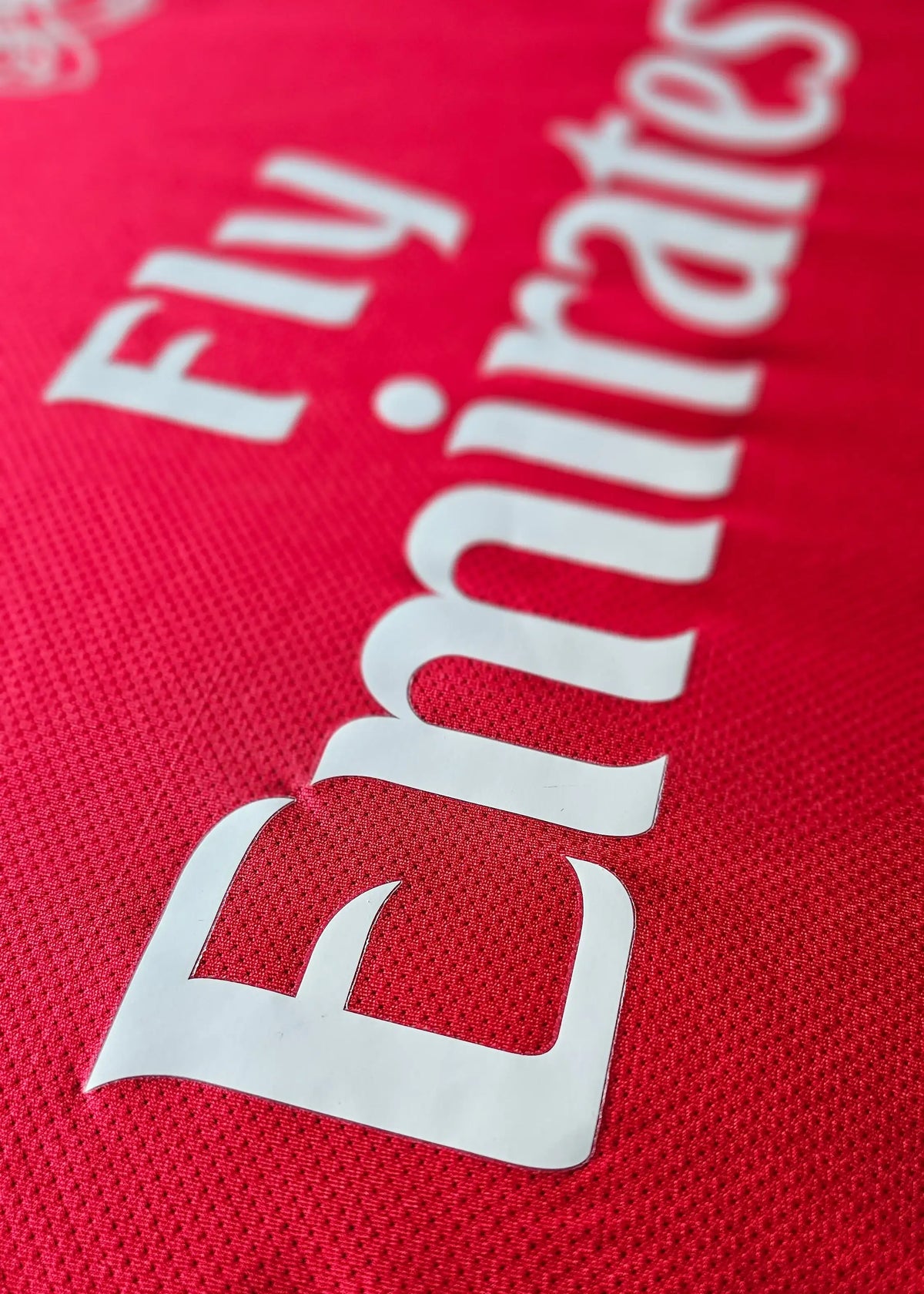 Fly Emirates sponsor lettering printed on red fabric, from Robin van Persie's signed Arsenal 2011-12 Champions League No. 10 shirt front.