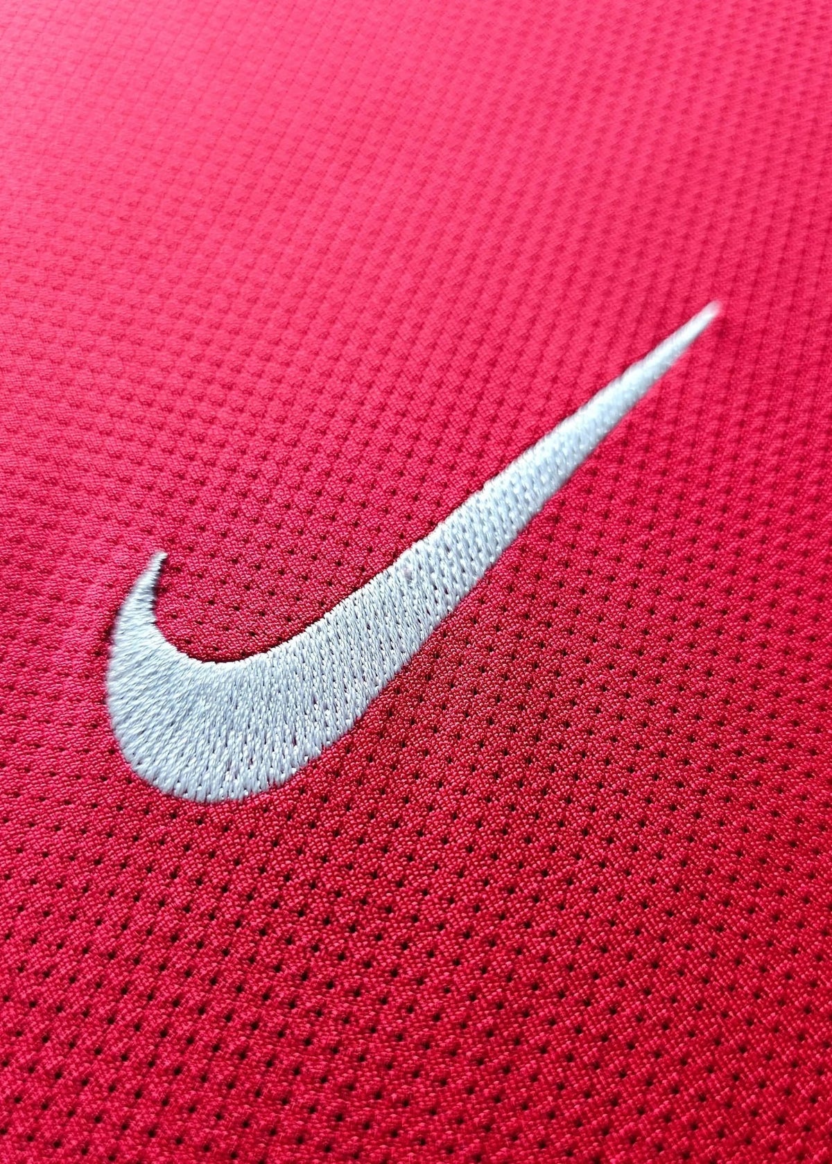 Close-up of the white Nike swoosh embroidered on red fabric, from Robin van Persie's signed Arsenal 2011-12 Champions League No. 10 shirt.