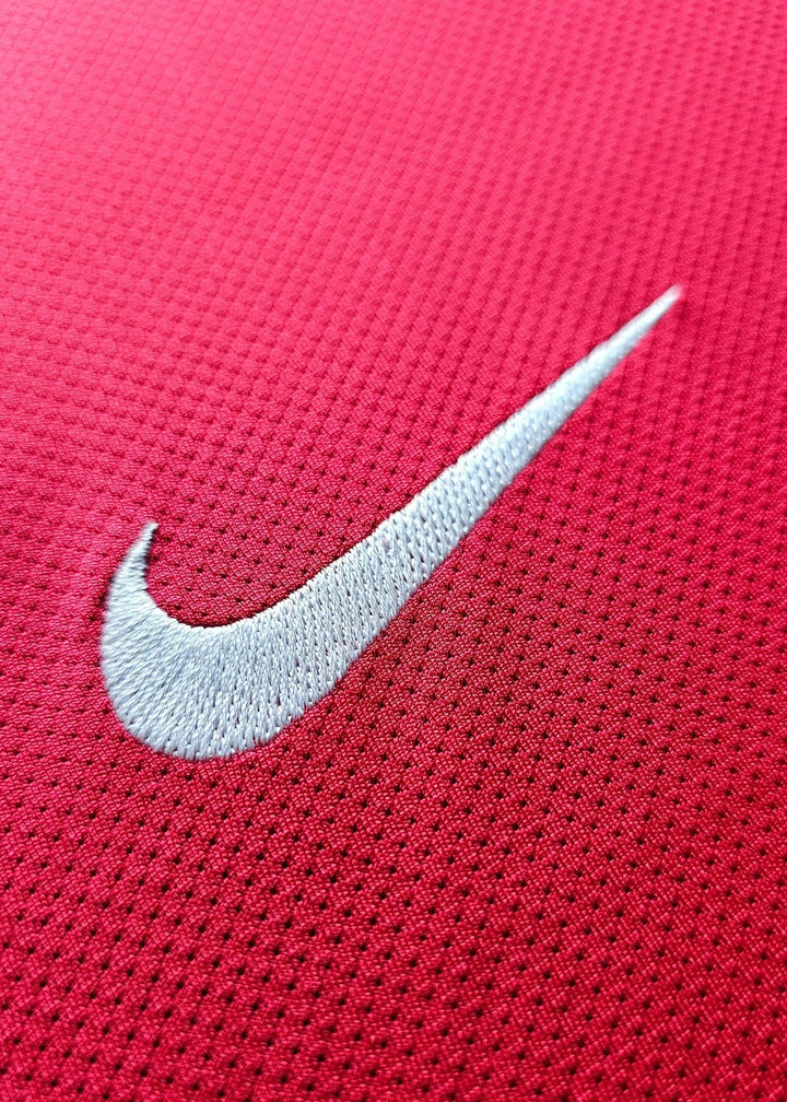 Close-up of the white Nike swoosh embroidered on red fabric, from Robin van Persie's signed Arsenal 2011-12 Champions League No. 10 shirt.