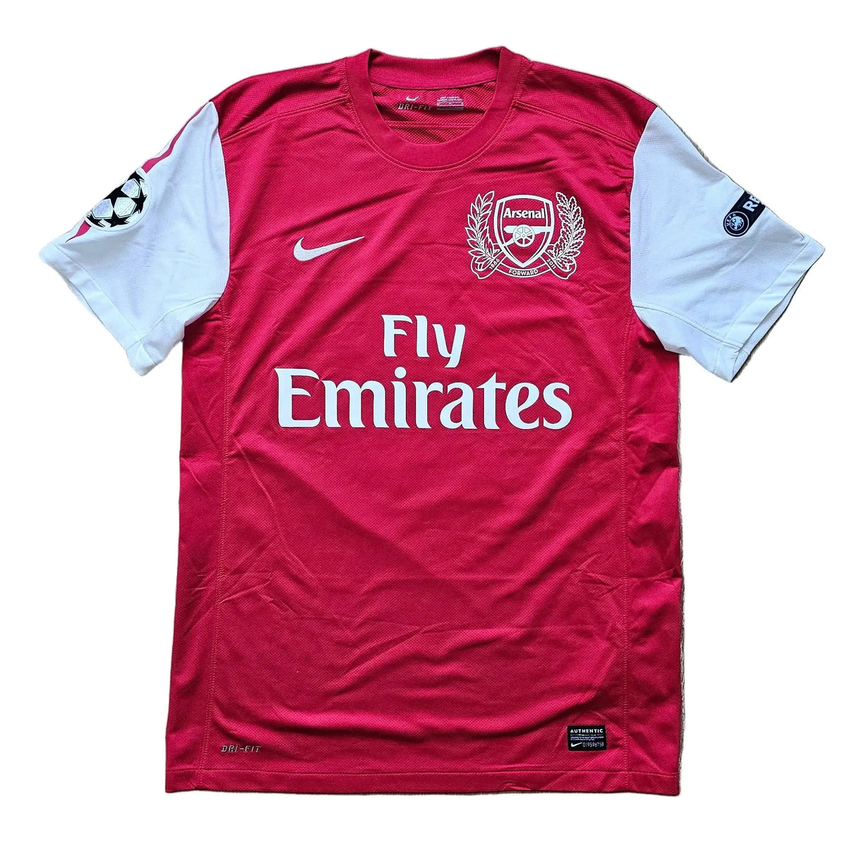 Front of a red and white Arsenal Champions League shirt with the Arsenal crest, Nike swoosh, Fly Emirates text, and UEFA sleeve patches, No. 10.