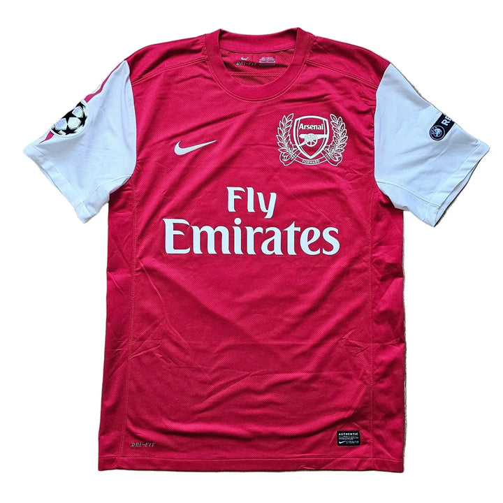 Front of a red and white Arsenal Champions League shirt with the Arsenal crest, Nike swoosh, Fly Emirates text, and UEFA sleeve patches, No. 10.