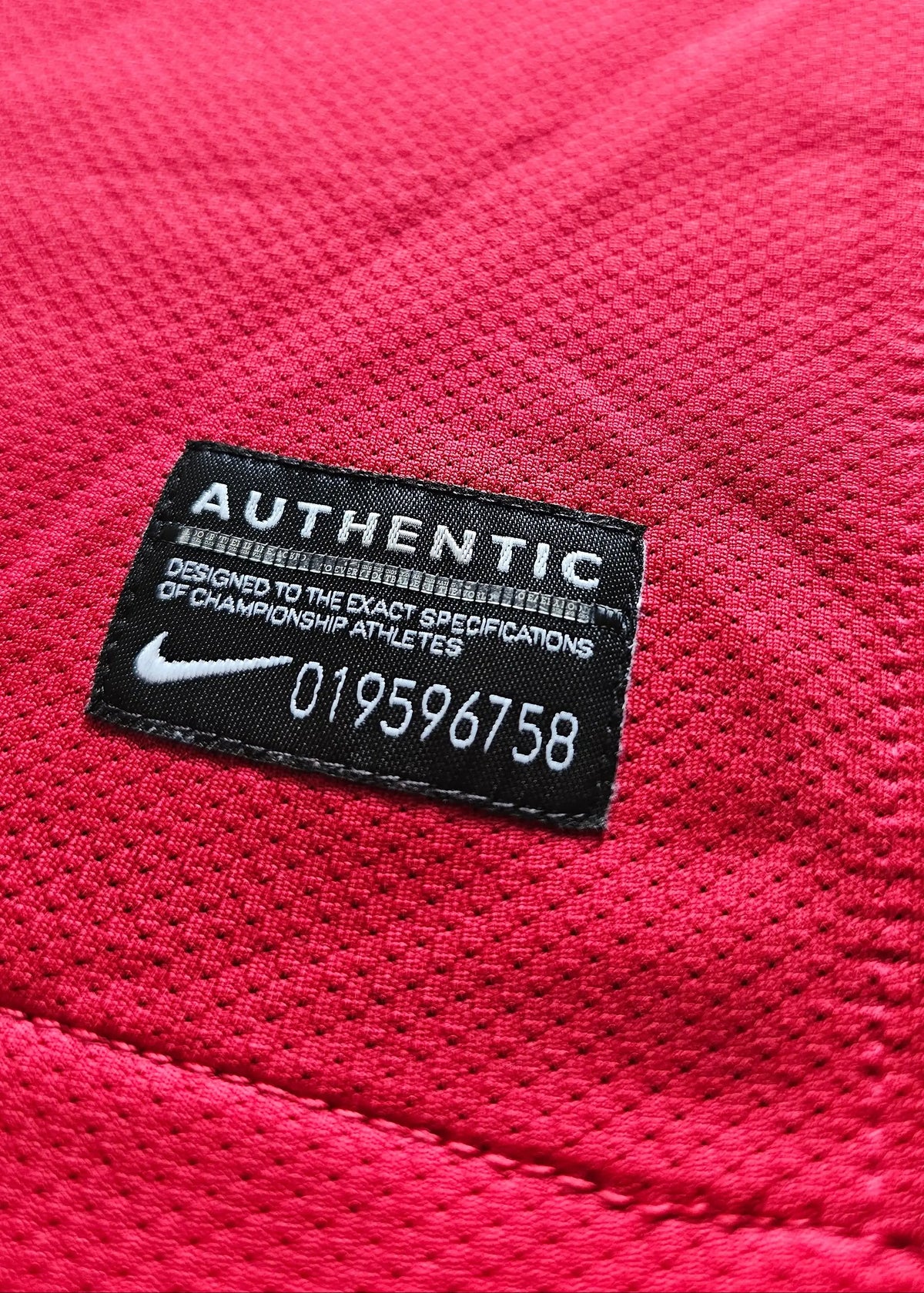 Nike Authentic tag with serial 019596758 on red mesh fabric, from Robin van Persie's signed Arsenal 2011-12 Champions League No. 10 shirt.