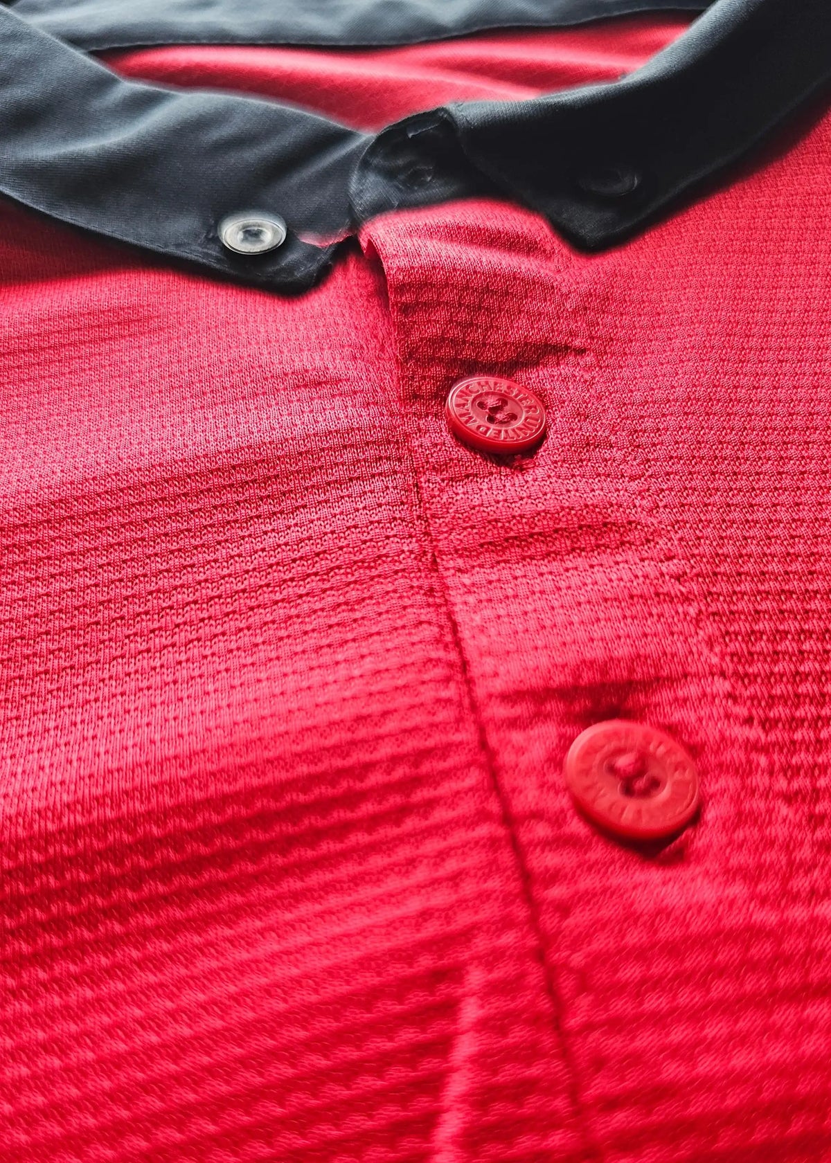 Close-up of red buttons embossed with Manchester United text on the black collar placket, Robin van Persie's signed 2014-15 No. 20 shirt.