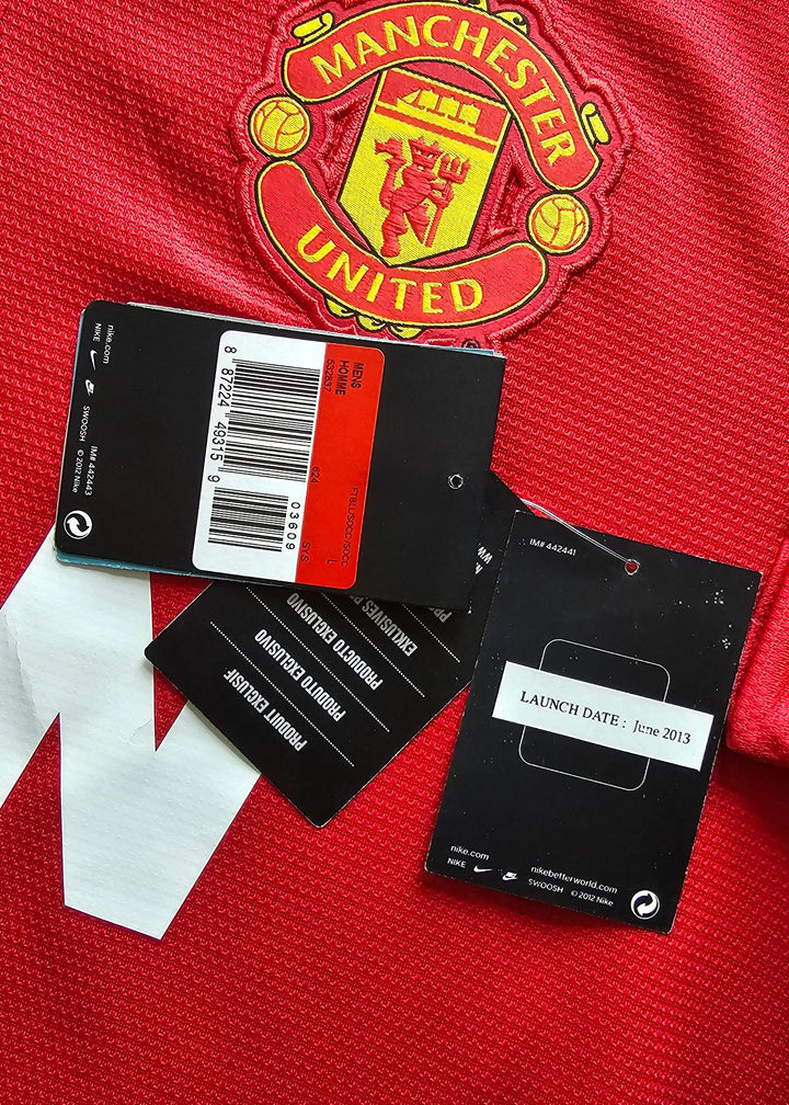Close-up of a red Manchester United soccer jersey with the club crest visible, along with black hang tags and a white size tag laid on the fabric.