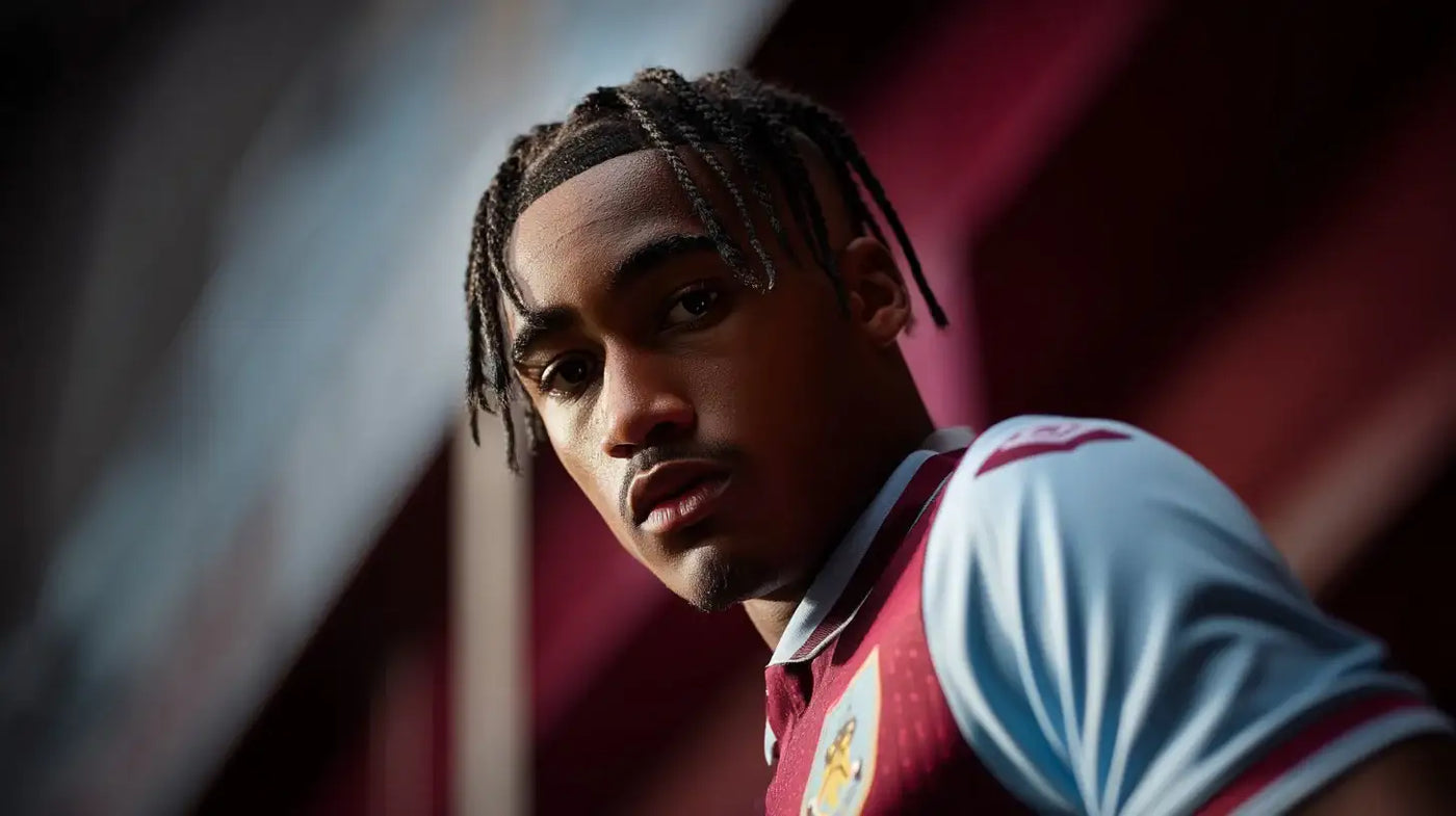 Wilson Odobert in a claret and sky blue Burnley home football shirt, close up, with blurred stadium seating in the background and a focused match-day expression.